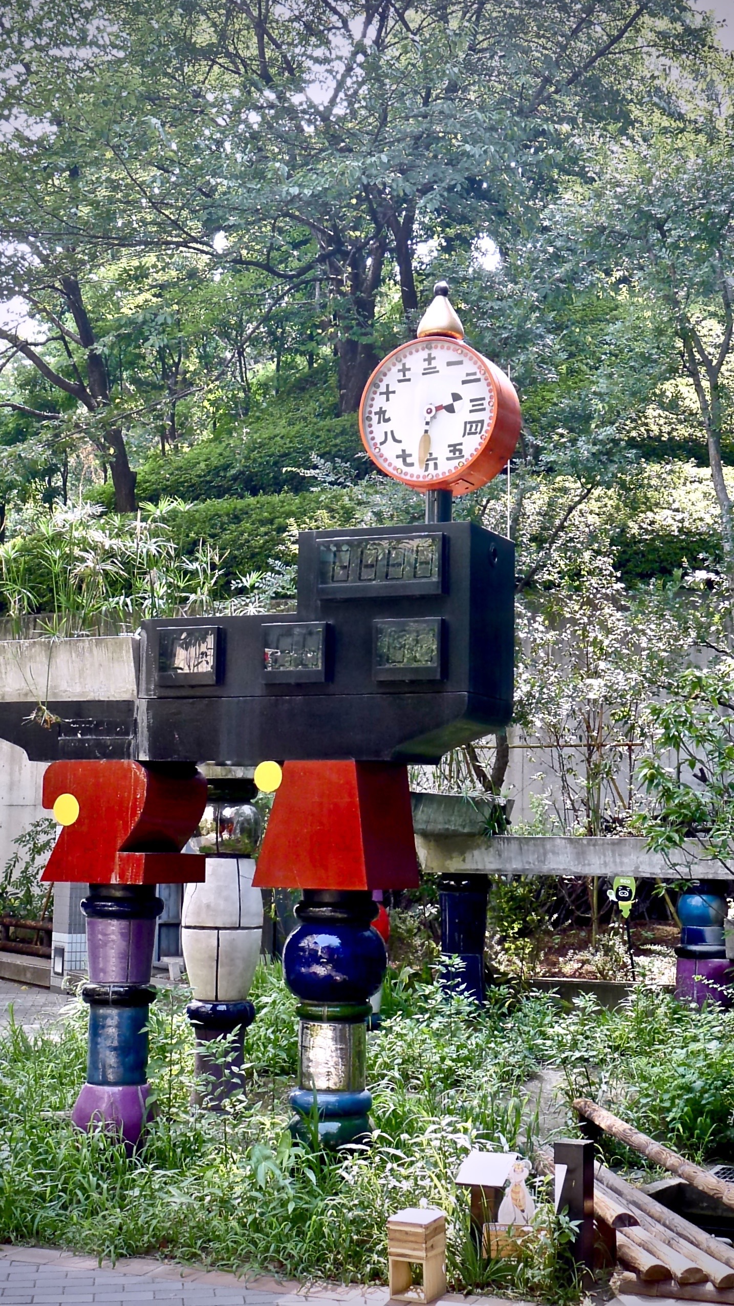 A vibrant outdoor sculpture with a clock is displayed in a garden setting.