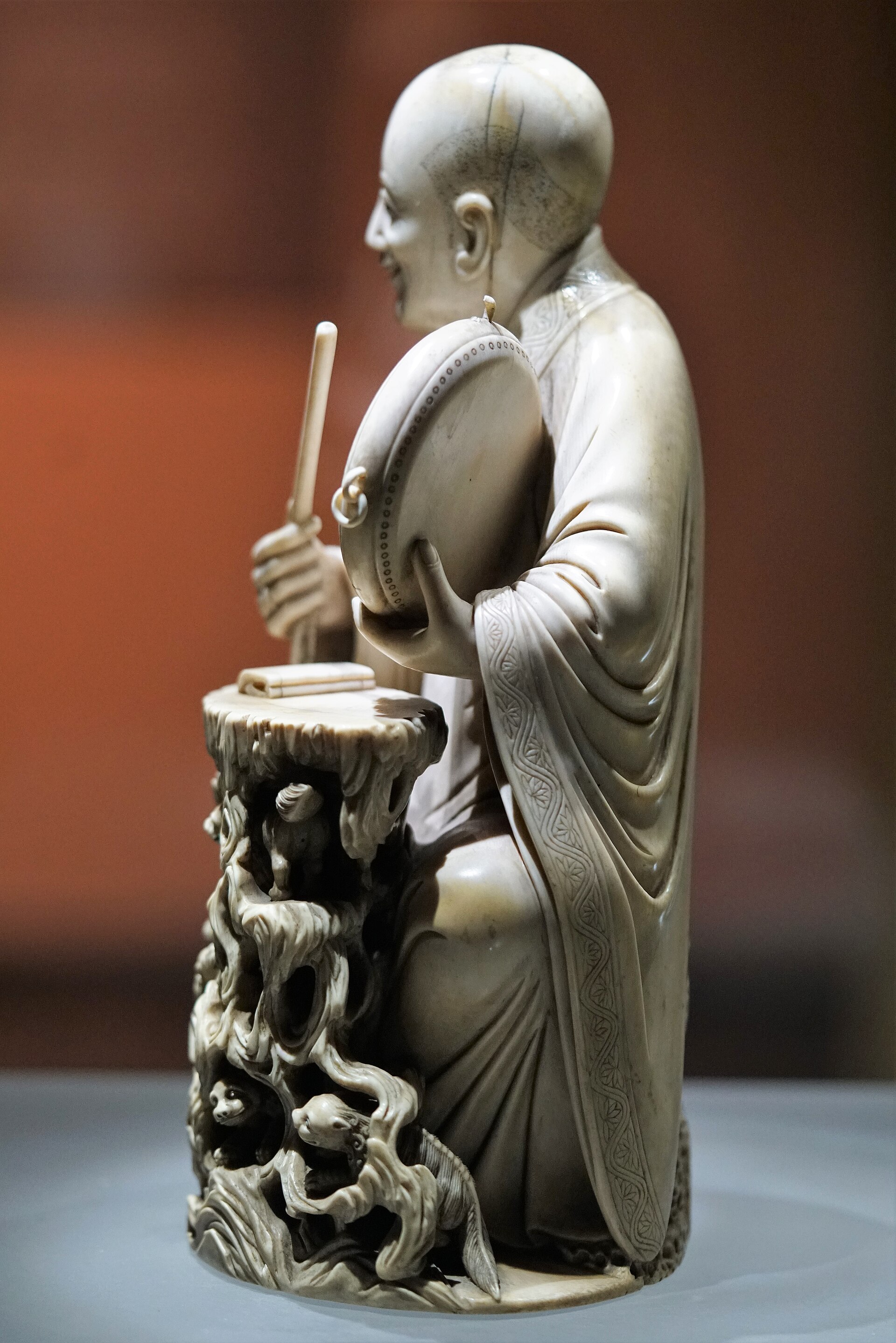 An intricately carved ivory statue depicts a seated monk playing musical instruments, reflecting the cultural context of.