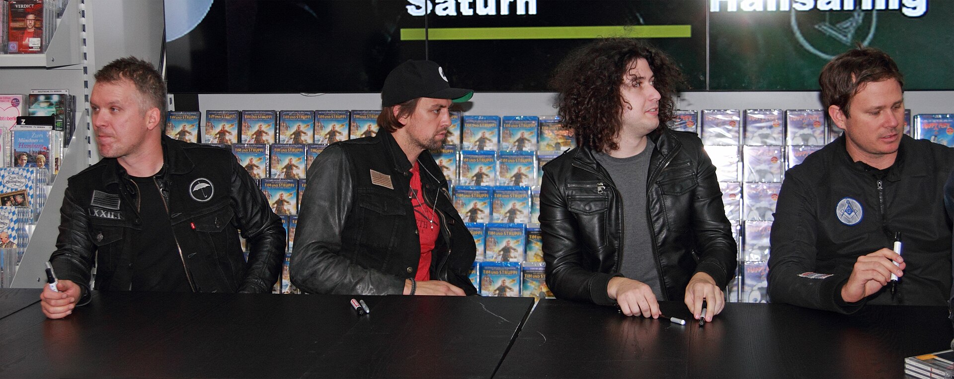 The Killers band members sign autographs during a music promotion event, showcasing the shift from print charts to airwaves.